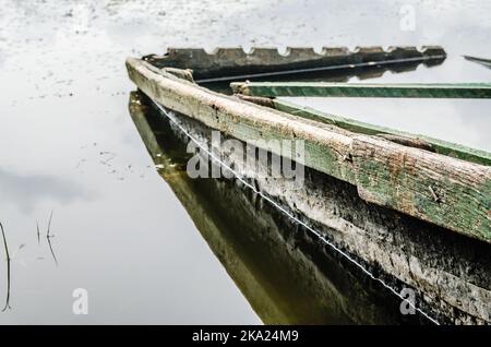 Bateaux de pêche en bois reliés à la rive. Une vue sur un petit bateau de pêche en bois abandonné, amarré au bord du lac en automne. Banque D'Images