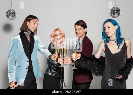 joyeux et élégant reines amis qui se trinquent des verres à champagne pendant la fête du nouvel an sur fond gris, image de stock Banque D'Images