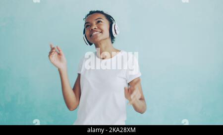 Portrait d'une femme afro-américaine heureuse écoutant de la musique à l'aide d'un casque sans fil et dansant en écoutant de la mélodie. Technologie moderne, jeunes et concept amusant. Banque D'Images