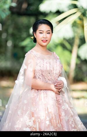 Fille asiatique dans une vieille rose rose couleur genou longueur robe molletonnée avec le talon élevé des chaussures à bride arrière et le fil de cérémonie sur son poignet. Elle est plus lumineuse Banque D'Images