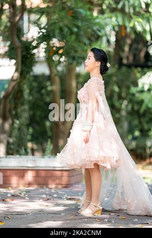 Fille asiatique dans une vieille rose rose couleur genou longueur robe molletonnée avec le talon élevé des chaussures à bride arrière et le fil de cérémonie sur son poignet. Elle est plus lumineuse Banque D'Images