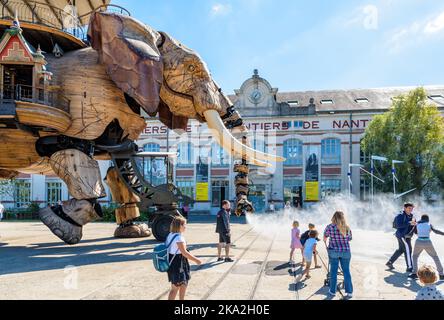 La marionnette géante du grand éléphant, qui fait partie des machines de l'île de Nantes, pulvérise de l'eau avec son tronc sur les spectateurs le long du bâtiment des chantiers navals. Banque D'Images