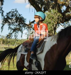 Un garçon caucasien portant un casque et un cheval dans un champ de verdure Banque D'Images