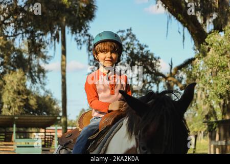 Un garçon caucasien portant un casque et un cheval dans un champ de verdure Banque D'Images