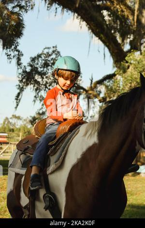 Un garçon caucasien portant un casque et un cheval dans un champ de verdure Banque D'Images