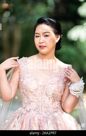 Fille asiatique dans une vieille rose rose couleur genou longueur robe molletonnée avec le talon élevé des chaussures à bride arrière et le fil de cérémonie sur son poignet. Elle est plus lumineuse Banque D'Images