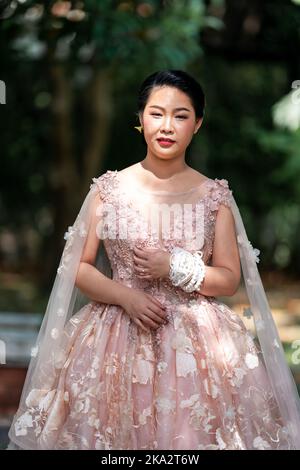 Fille asiatique dans une vieille rose rose couleur genou longueur robe molletonnée avec le talon élevé des chaussures à bride arrière et le fil de cérémonie sur son poignet. Elle est plus lumineuse Banque D'Images