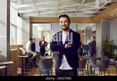 Portrait d'un homme d'affaires millénaire positif qui se pose sur fond de bureau moderne. Banque D'Images