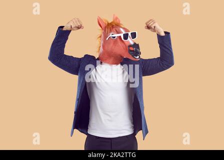 Homme en costume, drôle masque de cheval et lunettes de soleil montre sa force et fléchit ses bras Banque D'Images