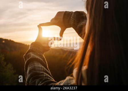 Concept de planification, de stratégie et de vision des affaires. Gros plan de la jeune femme faisant un geste de cadre avec un magnifique coucher de soleil dans les montagnes. Femme captur Banque D'Images