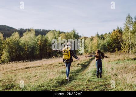 Drôle jeune mère caucasienne dans le chapeau et petite fille ludique enfant sont courir herbe, jouant pilote d'avion sur le ciel de fond et calme forêt d'automne. Tr Banque D'Images