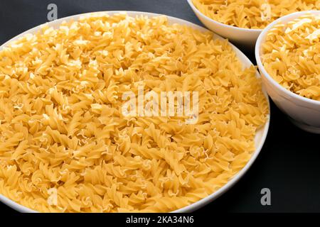 Pâtes Fusilli non cuites sur une plaque blanche sur fond noir.Macaroni cru et sec.Aliments malsains et gras Banque D'Images