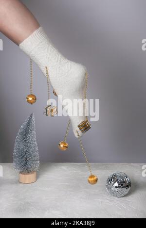 Un pied de femme dans une chaussette blanche décorée de jouets de Noël au-dessus de la scène avec un arbre de Noël artificiel en argent et une boule disco. Le concept de Banque D'Images