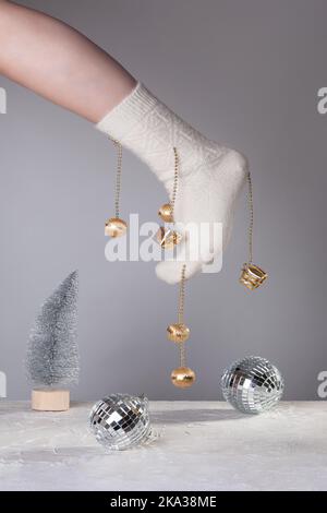 Un pied de femme dans une chaussette blanche décorée de jouets de Noël au-dessus de la scène avec un arbre de Noël artificiel en argent et des boules disco. Le concept de Banque D'Images