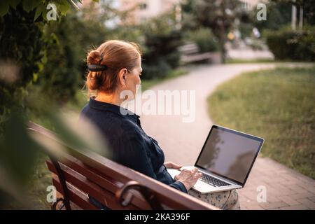 Femme d'affaires mature utilisant un ordinateur portable assis sur un banc dans le parc Banque D'Images