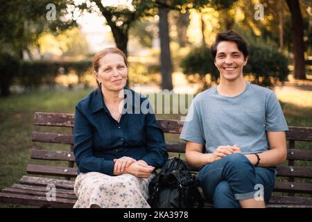 Bonne mère mûre et un fils adulte souriant assis sur le banc dans le parc Banque D'Images