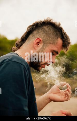 Un jeune gars qui fume un joint de marijuana tout en le regardant Banque D'Images