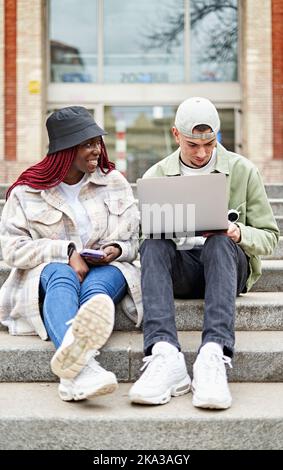 Couple assis dans les escaliers à l'université et travaillant sur ordinateur portable Banque D'Images