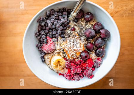 Dessus plat en regardant vers le bas sur le petit déjeuner avoine porridge bol avec beurre d'arachide, baies congelées framboises bleuets et cerises avec banane Banque D'Images