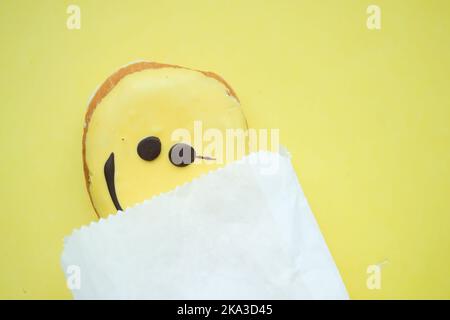 motif visage souriant, beignet et paquet sur fond jaune Banque D'Images