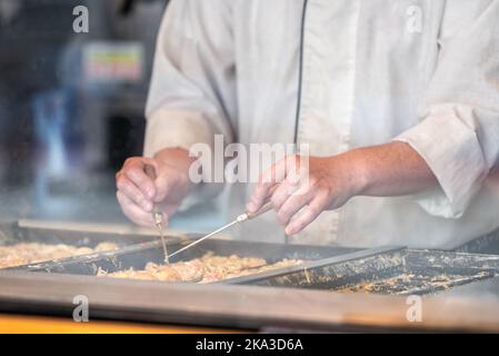 Gros plan de l'homme chef personne qui cuisine en retournant au-dessus des boules de poulpes japonais takoyaki cuisine de rue avec des pelles en acier à Ginza, Tokyo Japon Banque D'Images