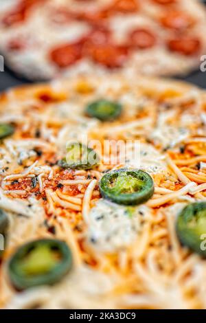 Macro gros plan vue verticale des crus non cuits prendre et cuire au four du poivre congelé fromage mozzarella râpé et de la tarte à la pizza au jalapeno sur un plateau prêt à cuire Banque D'Images