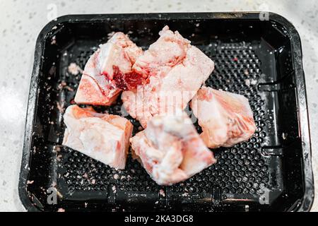 Macro-gros plan des os de la moelle de boeuf dans un contenant de plateau d'emballage noir avec de la viande brute non cuite rouge isolée sur fond blanc Banque D'Images