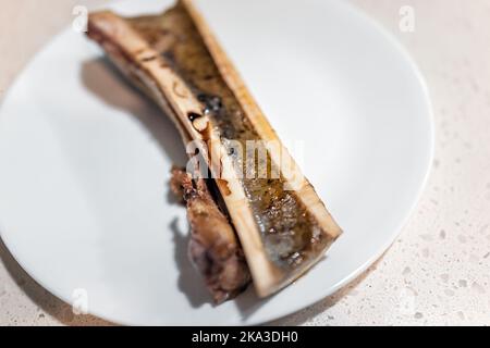 Macro-gros plan d'une moitié d'os de moelle de bœuf cuit au four divisé en deux sur l'assiette à la table de cuisine avec le collagène gras liquide isolé contre le bac blanc Banque D'Images