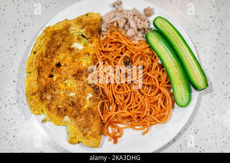 Omelette au fromage frais et chaude avec concombres légumes, viande de poulet de porc tirée et nouilles asiatiques pâtes frites sur une plaque blanche cuite pour le tradi du matin Banque D'Images