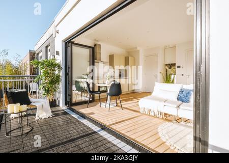 Porte ouverte du balcon dans le salon contemporain lumineux avec canapé et parquet près de la cuisine moderne en journée Banque D'Images