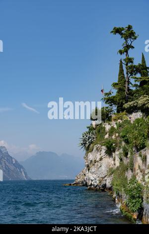 Une vue panoramique sur les plantes sauvages et les arbres sur la falaise du lac de Garde avec des montagnes à l'horizon contre le ciel bleu en plein soleil, Italie Banque D'Images