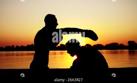 Deux hommes noirs, au lever du soleil, contre la lumière, la boxe, les combats en partrain, formation dans une paire de techniques de grèves. Sur la plage de sable, dans le port de cargaison, près de l'eau, en été. Photo de haute qualité Banque D'Images