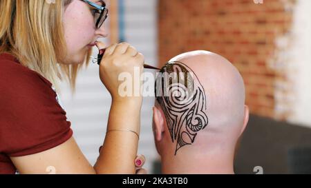 Un gros plan, l'exécution d'un maître, un artiste mehendi, un tatouage, une photo de henné sur le cuir chevelu blanc, un homme blanc de race blanche. Ornements abstraits noirs et marron foncé. Photo de haute qualité Banque D'Images