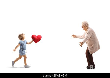 Photo pleine longueur d'une petite fille qui court à une femme âgée et porte un cœur rouge isolé sur fond blanc Banque D'Images