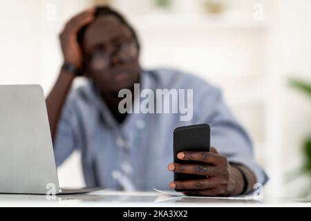 Jeune Afro-américain utilisant un téléphone intelligent tout en étant assis au bureau dans le bureau Banque D'Images
