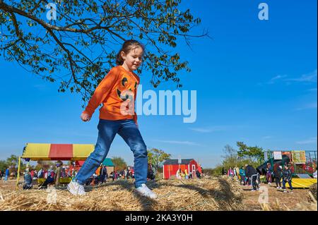 Jolie fille sautant sur les piles de foin à une foire agricole sur Halloween Banque D'Images