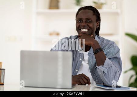 Portrait du jeune homme afro-américain souriant posé au bureau avec un ordinateur portable Banque D'Images