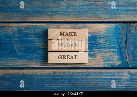 Créez une excellente affiche aujourd'hui sur trois chevilles en bois empilées placées sur un fond bleu texturé. Banque D'Images