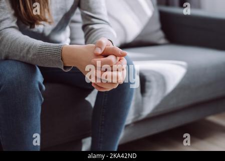 Une femme méconnaissable se replie les mains sur les genoux ensemble, assise sur un canapé seul, contrariée, la fille déprimée se sentant seule, souffrant de violence domestique ou Banque D'Images