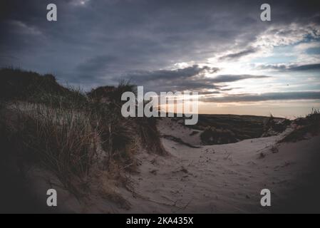 Un immense paysage de nuages sur des dunes de sable herbacées pendant le coucher du soleil Banque D'Images