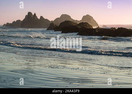 Lever ou coucher de soleil sur la côte de l'Oregon, avec des vagues se lavant au-dessus de rockers rugueux pour atteindre la plage de sable. Banque D'Images