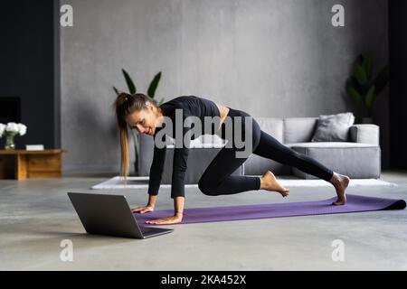 Femme sportive concentré durables est en train de faire l'élaboration à la maison et faisant partie de l'avant de son ordinateur portable, le port de vêtements de sport Banque D'Images