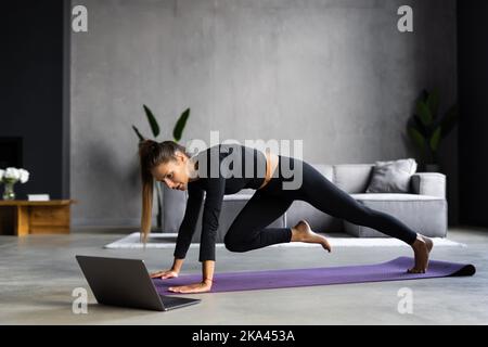 Femme sportive concentré durables est en train de faire l'élaboration à la maison et faisant partie de l'avant de son ordinateur portable, le port de vêtements de sport Banque D'Images