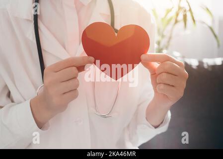 Gros plan de la jeune femme médecin vêtue d'un uniforme blanc et stéthoscope tenant le papier rouge assis dans un canapé confortable à la clinique. Concept d'assurance maladie, wor Banque D'Images