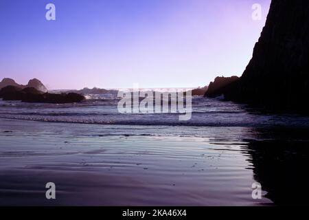 Lever ou coucher de soleil sur la côte de l'Oregon, avec des vagues se lavant au-dessus de rockers rugueux pour atteindre la plage de sable. Banque D'Images