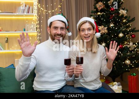 Couple mature homme et femme mariés célébrant Noël et nouvel an ensemble, regardant la webcam et souriant parlant à des amis lors d'un appel vidéo tenant des verres à vin dans les mains en signe de salut à la maison Banque D'Images