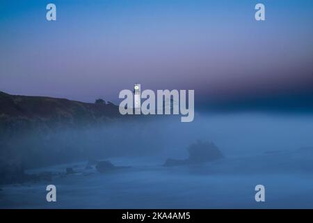 Lever de soleil au phare de Yaquina Head à Newport, Oregon. Le phare est sur un affleurement rocheux, avec la mer en dessous avec une couche de brouillard sur le bea Banque D'Images