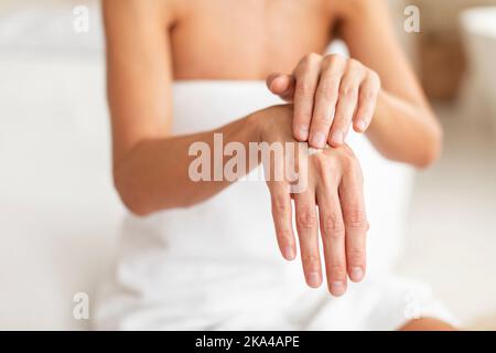 Gros plan d'une femme d'âge moyen appliquant une goutte de crème hydratante sur les mains, en utilisant une lotion nourrissante pour la peau sèche Banque D'Images