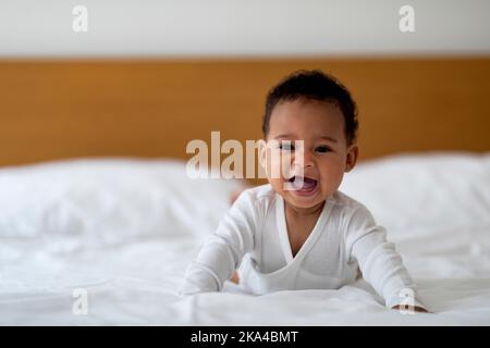 Adorable petit Afro-américain bébé portant Bodysuit rampant sur le lit à la maison Banque D'Images