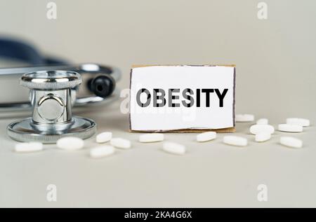 Concept médical. Sur fond gris, un stéthoscope, des pilules et une plaque en carton avec l'inscription "obésité" Banque D'Images